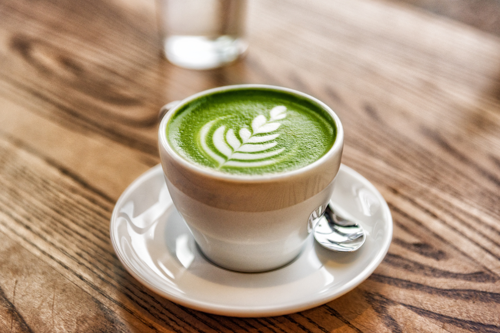 Cup of matcha latte with green foam and latte art on a wooden table.