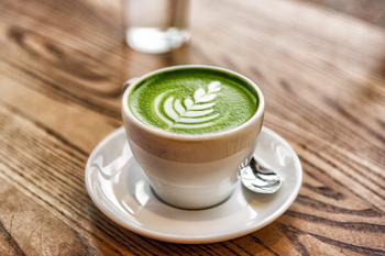 Cup of matcha latte with green foam and latte art on a wooden table.