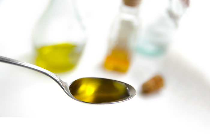 Spoonful of extra virgin olive oil with bottles in background