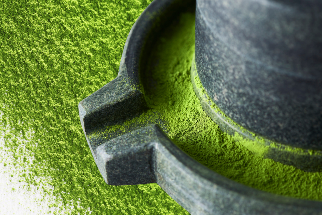Traditional stone mill grinding vibrant green matcha powder.