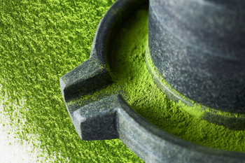 Traditional stone mill grinding vibrant green matcha powder.