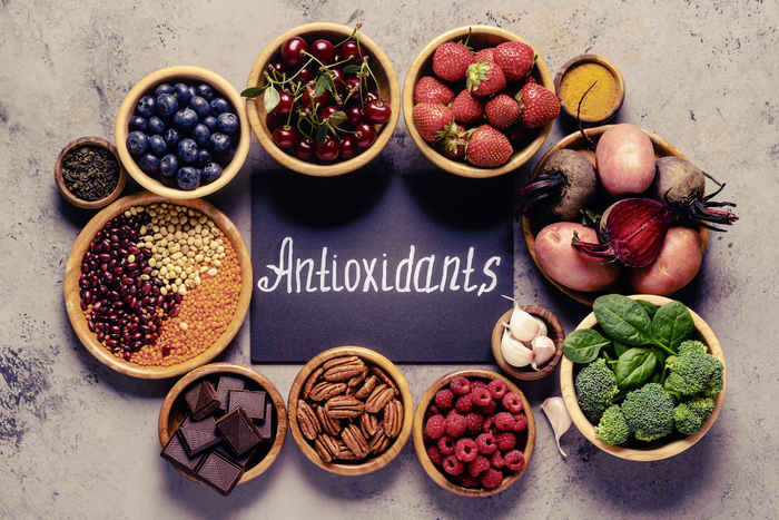 Assorted antioxidant foods including berries, leafy greens, dark chocolate, and legumes arranged around a chalkboard labeled “Antioxidants.”