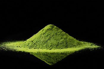Pile of bright green matcha powder on a reflective black surface.
