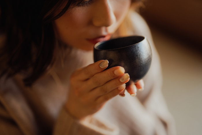 Woman holding and sipping from a black tea cup during a quiet matcha meditation ritual.