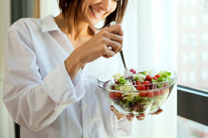 Woman smiling while eating a fresh vegetable salad near a window
