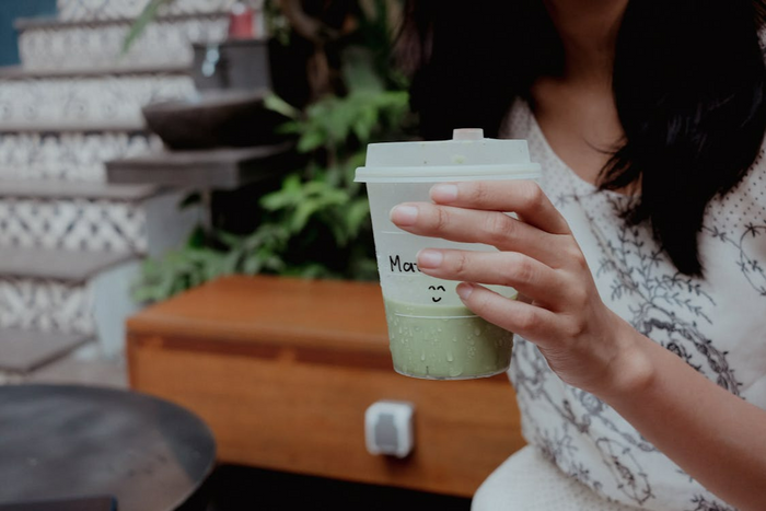 Close-up of a woman holding a cup of matcha latte with a smiley face