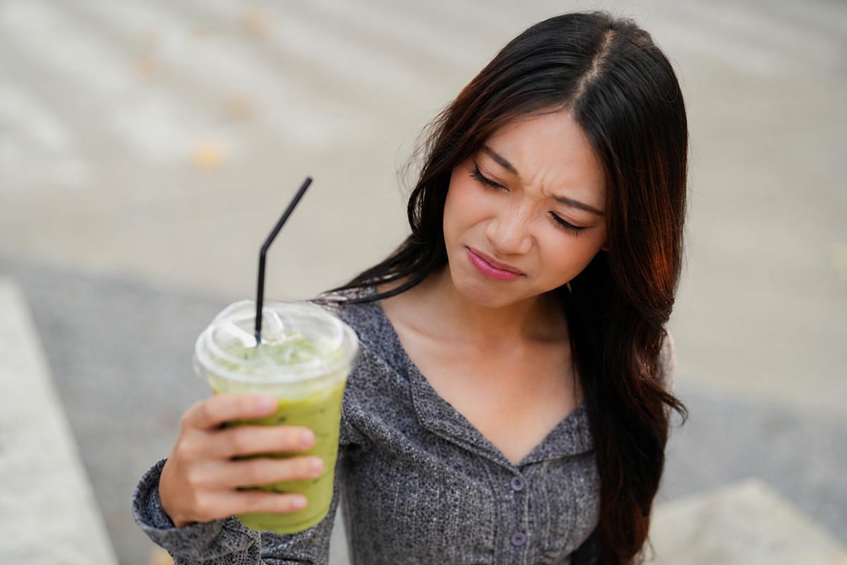 Woman making a bitter face while holding a cold green matcha drink.