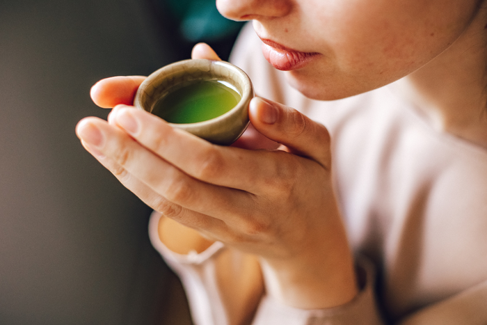 Woman gently sipping freshly whisked matcha green tea from a small ceramic cup