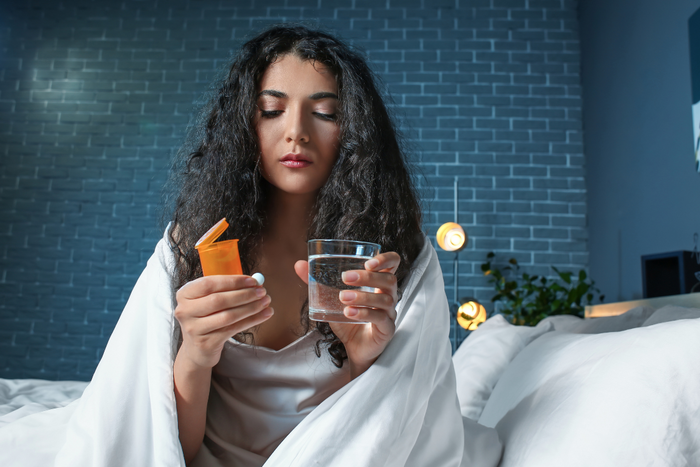 Woman sitting in bed at night holding a pill and glass of water, preparing to take a supplement.